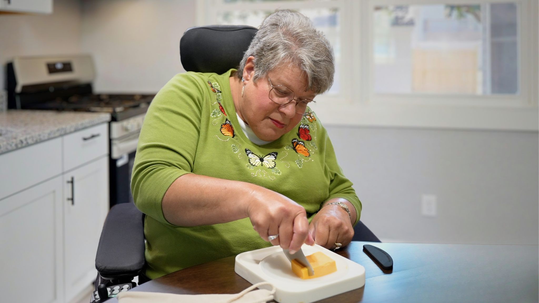 A smiling adult using the Holstead meal prep tool to cut cheese one-handed